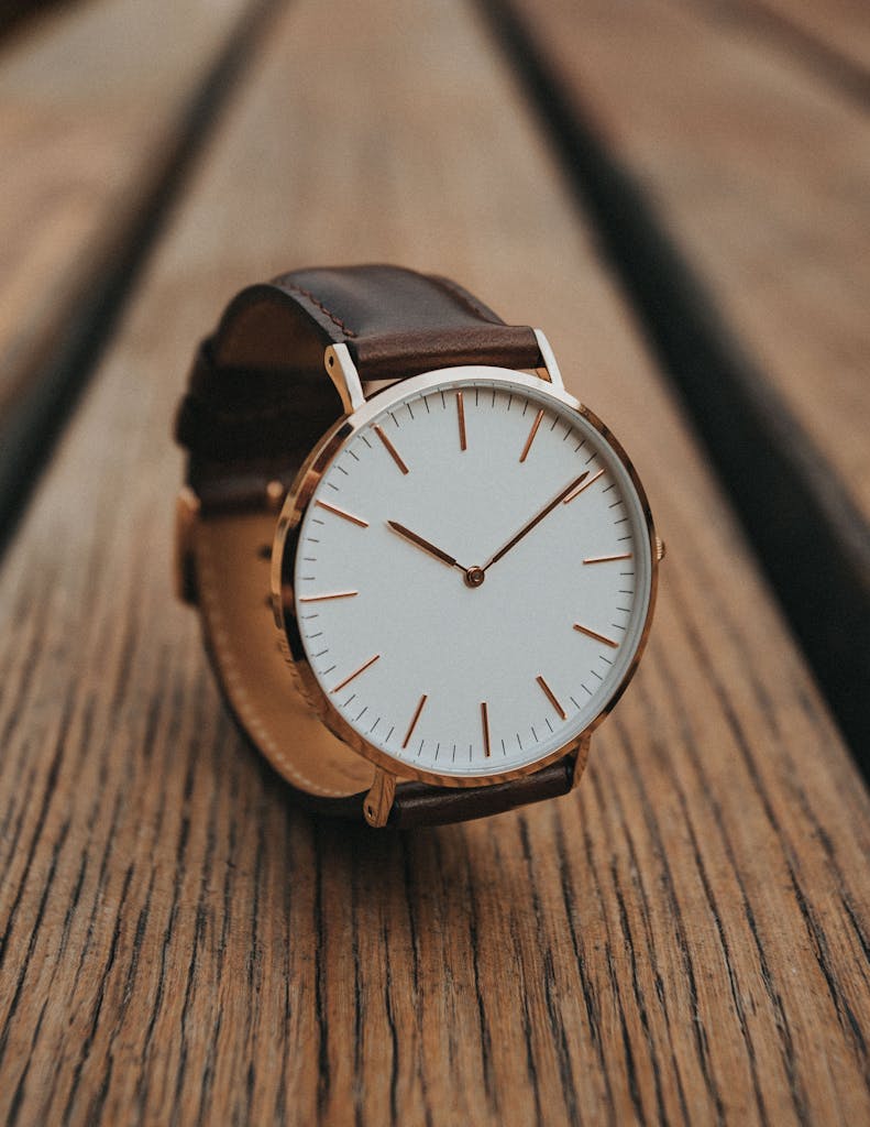 Close-up of a minimalist analog watch with brown leather strap on a wooden surface.